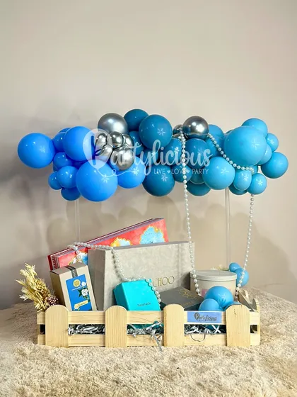 A beautiful baby boy gift hamper, with a blue balloon cloud floating above a crate of carefully selected presents.