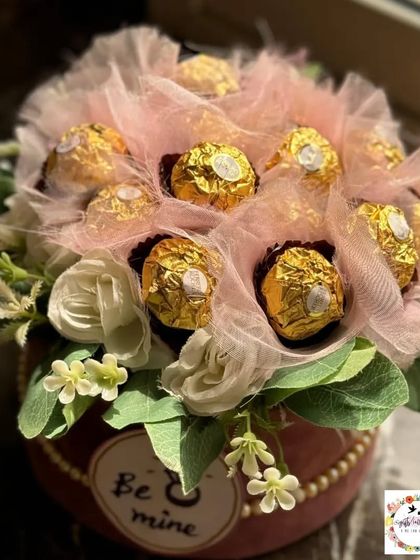 A still shot of the custom chocolate bouquet, highlighting the arrangement of Ferrero Rocher chocolates nestled in pink tulle and surrounded by white artificial roses. This is a perfect addition to any engagement or bridal hamper.