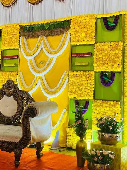 A bright and cheerful Seemantham backdrop with a yellow and green theme. The design features panels of marigolds and is decorated with intricate white floral garlands.