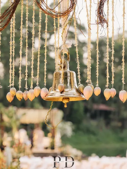 A detail shot of the traditional brass bell hanging within the floral canopy of the South Indian mandap. These small touches add authenticity and charm to the overall design.