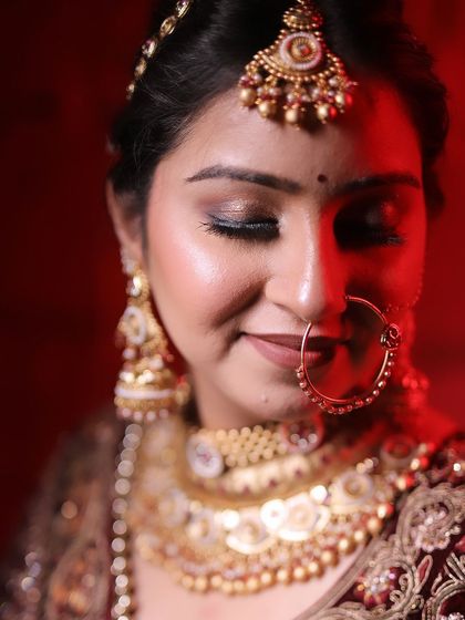 A close-up portrait of a bride under dramatic red lighting, highlighting her makeup and jewelry.