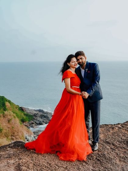 A stunning wide shot of a couple on a cliff, with the red gown's train spread out. It's a perfect example of a dramatic and beautiful pre-wedding photo.