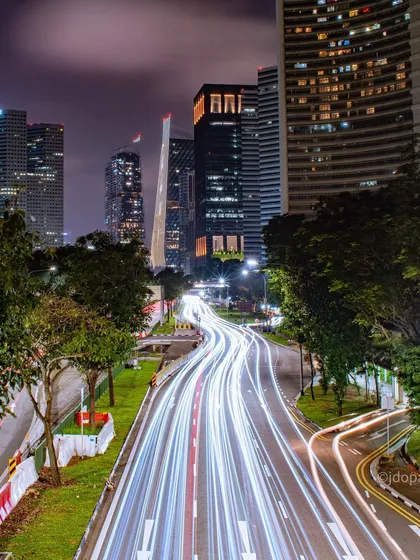 A long exposure photograph of a Singaporean highway, where the streaks of vehicle lights create a sense of speed and energy against the modern city architecture. This technique reveals the structured flow of urban life after dark.