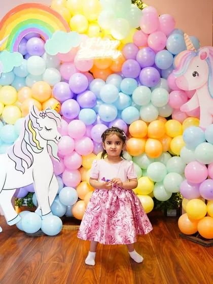 The birthday girl poses in front of her pastel rainbow balloon wall, a beautiful and popular choice for unicorn and magical themes.