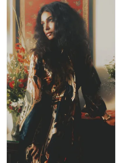 A portrait from 'Roots' where the model is bathed in soft, warm light. The voluminous hair and layered styling contribute to the rich, textured feel of the editorial.