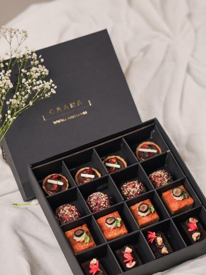 Our Rakhi Re-Imagined sweet box, filled with sixteen modern Indian bites, is a perfect gift to share. The elegant black box is adorned with baby's breath, adding a delicate touch.