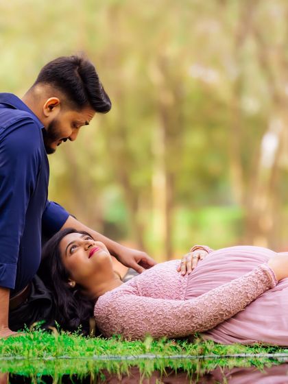 A serene moment by the water. The expecting mother lies on the grass while her partner watches over her, creating a peaceful and romantic pregnancy portrait.