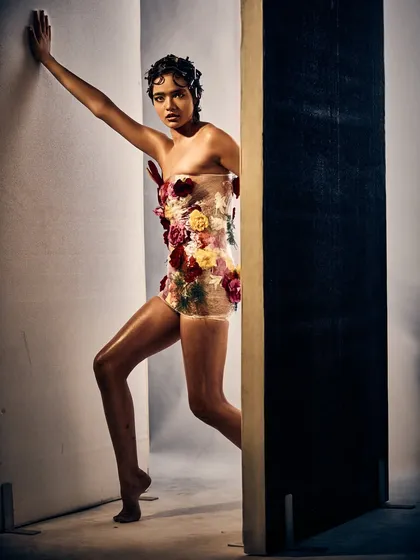Here, the floral couture and dewy skin create a striking contrast against the stark, geometric background. The pose and the look work together to tell a story of being confined yet powerful.