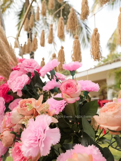 A close-up of a dreamy Mehndi arch, showcasing the beautiful texture of pink carnations, roses, and jute tassels.