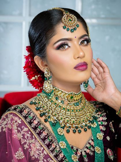 This bridal portrait highlights the beauty of contrast, pairing a deep velvet lehenga with striking emerald green jewelry. The makeup features a sharp wing and a bold lip to complete the powerful look.