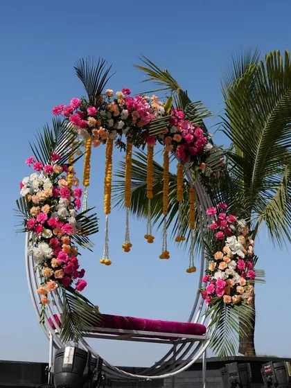 A stylish and modern seating arrangement for a Haldi ceremony. The circular floral wreath swing provides a perfect photo opportunity against the bright blue sky.