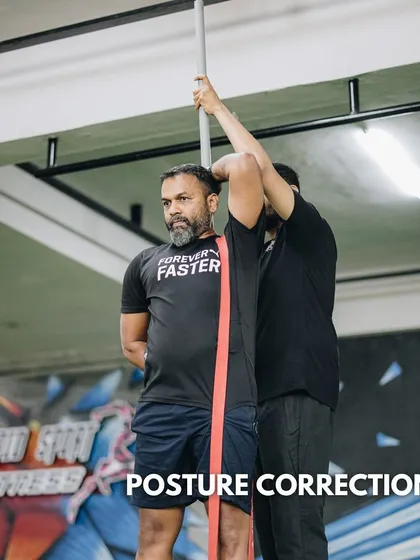 We use targeted exercises and tools to improve posture. A coach assists a client with a resistance band drill to correct alignment and strengthen postural muscles.