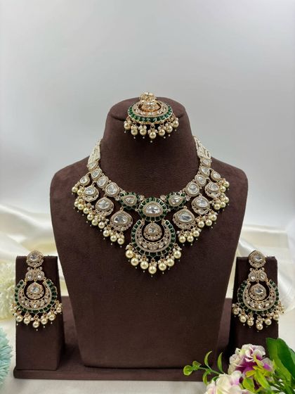 One of our most requested bridal sets, this design features large uncut Kundan stones, green Meenakari work, and pearl detailing. The set includes a necklace, chandbali earrings, and a matching maang tikka.