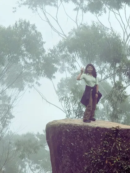 A traveler posing on the edge of a cliff in Kodaikanal, with the misty forest as a backdrop.