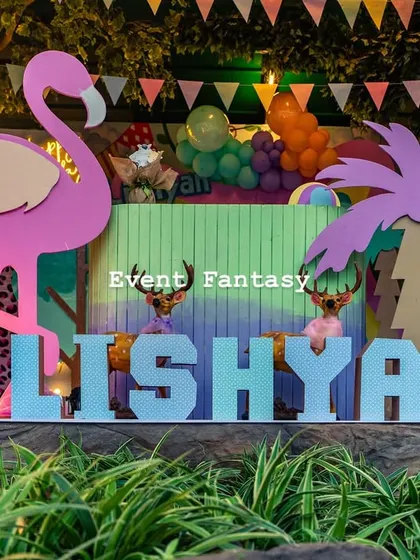 A close-up of the custom "LISHYAN" name display in pastel blue, set against a backdrop of lush greenery and party decorations.