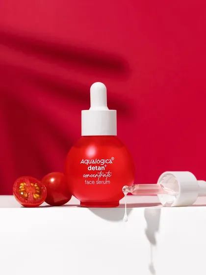 Bold and graphic. This shot uses a strong red background and dramatic shadows to highlight the detan serum. The inclusion of fresh cherry tomatoes connects the product directly to its natural ingredients.