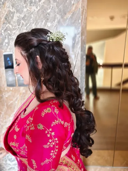 A detailed view of a romantic and intricate hairstyle. This half-up, half-down look combines soft, voluminous curls with a delicate braid, accented with baby's breath flowers for a touch of whimsy, ideal for any wedding event.