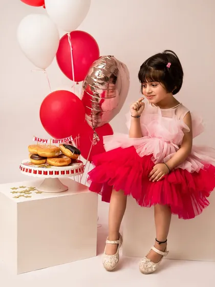 A quiet, thoughtful moment during her 4th birthday celebration. Dressed in a pink and red tulle dress, she looks like a little princess contemplating her birthday donuts.
