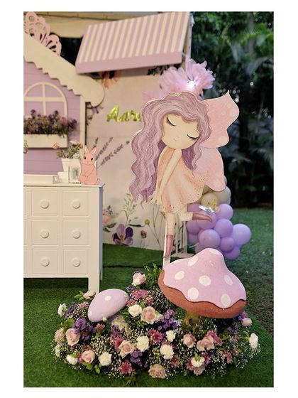 A beautiful fairy prop stands amidst a garden of flowers and a whimsical mushroom, part of our detailed enchanted party setups.