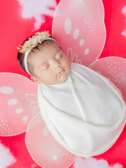 A close-up of a newborn wrapped snugly, with delicate butterfly wings against a vibrant red backdrop.