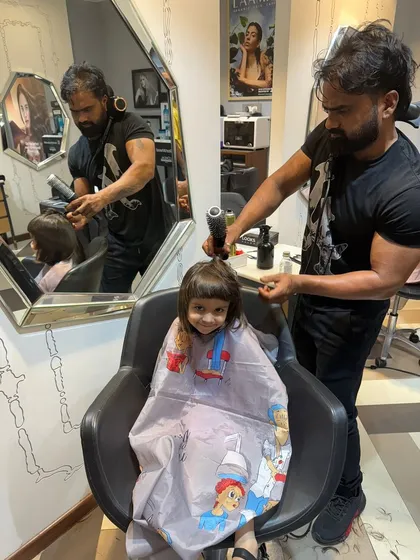 A happy little girl smiling in the salon chair while getting her bangs trimmed. We make sure our youngest clients have a fun and comfortable experience.
