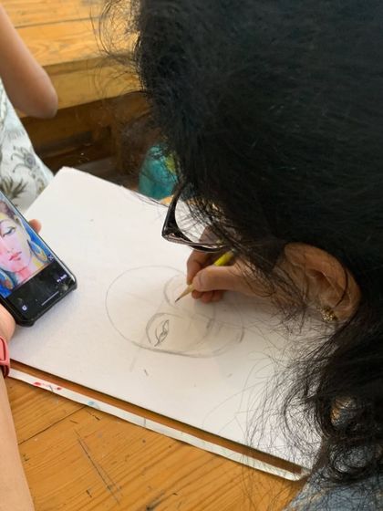 The journey begins with a sketch. Here, a student carefully draws the outline of a Buddha portrait before beginning the watercolor process.