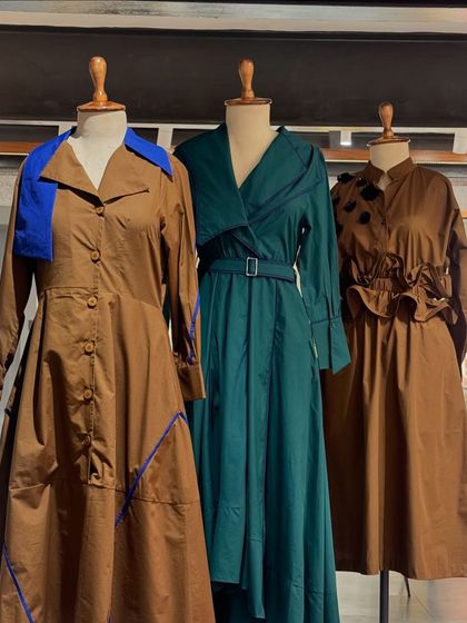 A trio of structured outfits, including a brown trench coat with blue accents and a belted green dress, showcasing sharp tailoring.