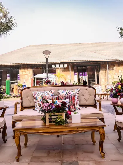 Another seating area from the Rajasthani-themed Mehendi, featuring elegant wooden furniture with colorful printed cushions, blending rustic charm with vibrant accents.