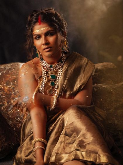 The dramatic lighting and rugged setting provide a stark contrast to the shimmer of the golden saree in this editorial shot.