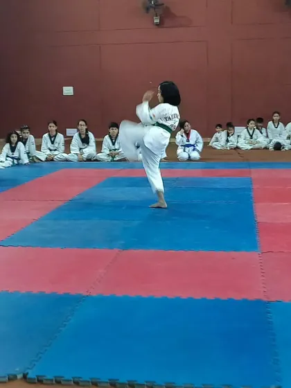 A young girl performs a solo Taekwondo kicking form on the training mats. This showcases her balance and technique in front of her fellow students, building performance confidence.
