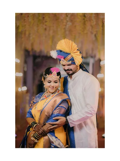 The groom lovingly embraces his bride during their Maharashtrian lagn. Her traditional mundavalya and his pheta are key elements of their beautiful wedding look.
