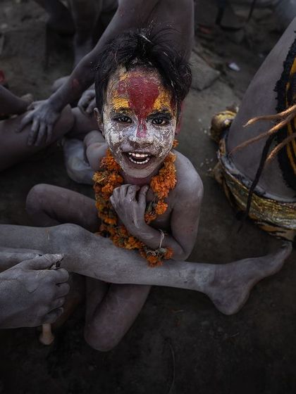 A high-angle shot of a smiling child covered in ash and paint during a festival in Varanasi, capturing the uninhibited joy of the moment.