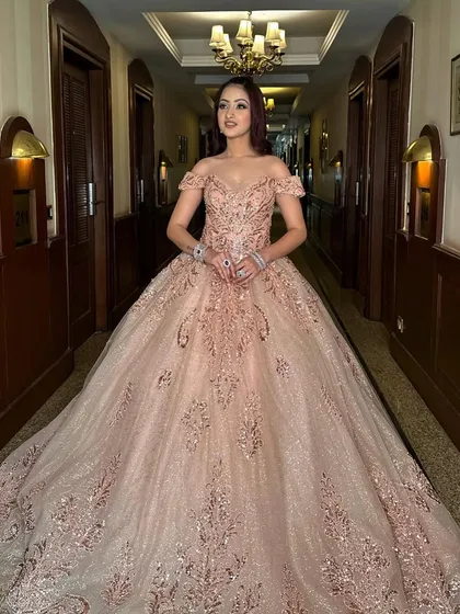 A full-length shot of our rose gold Cinderella ball gown in a grand hallway. The gown's voluminous skirt and sparkling embroidery make it the perfect choice for a dramatic and elegant entrance.