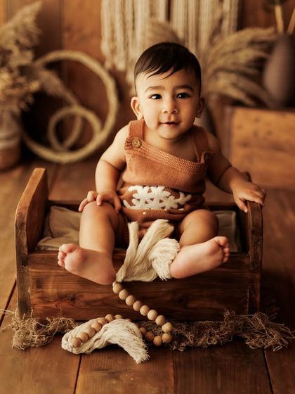 A heartfelt happiness that lights up the room. This little one is sitting up on the wooden bed, holding a string of beads and looking so proud.