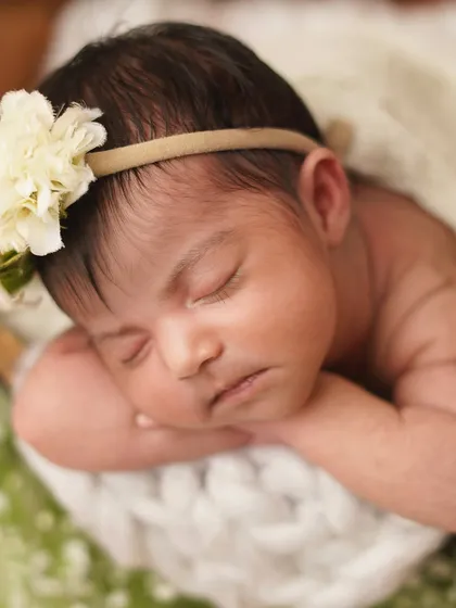 A sweet close-up of a newborn resting her head on her hands. The soft lighting and floral details enhance the dreamy quality of this infant portrait.