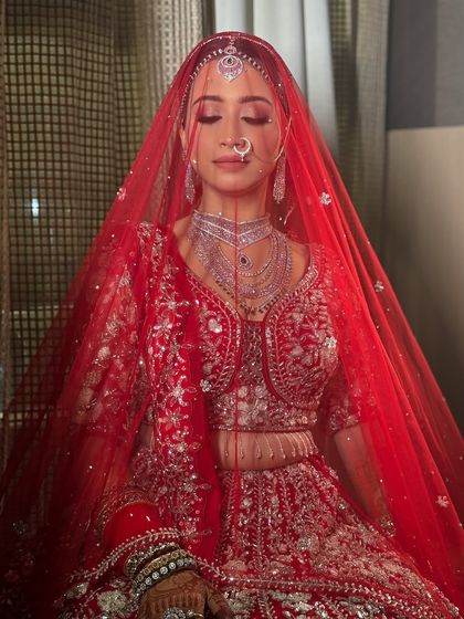 A beautiful, serene portrait of the bride under her red veil. The soft lighting creates an ethereal glow, highlighting her flawless makeup.