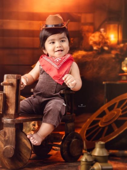 Another little cowboy ready for the rodeo, dressed in a brown hat and red bandana in a warm, rustic setting.