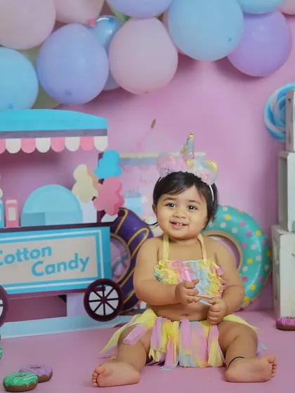 A happy one-year-old in her colorful candyland setup. The unicorn headband and pastel dress complete this adorable first birthday look.