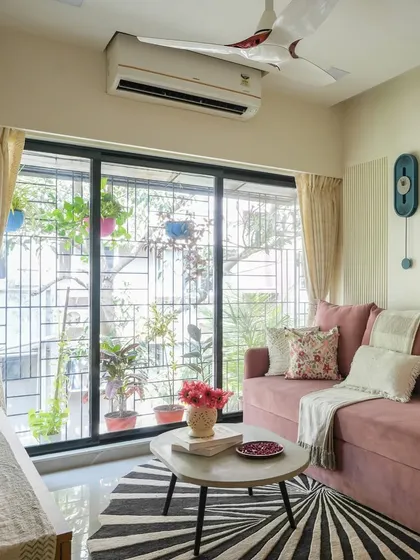 A dusty rose sofa brings a gentle warmth to this living room. Paired with a bold, graphic rug and a balcony garden view, the space feels fresh, modern, and full of life.