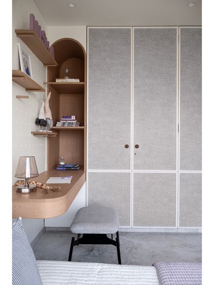 This view shows the study area next to the fabric-paneled wardrobes. The arched shelving and curved desk create a soft, inviting workspace that is seamlessly integrated into the room's design.