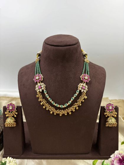The Rishika premium antique gold set. It features a unique double-layer design with one layer of golden beads and another of green beads, adorned with floral motifs in pink stones.