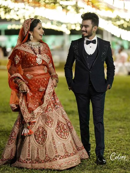 A full-length shot of a couple in their wedding attire, sharing a laugh in a garden setting at night.