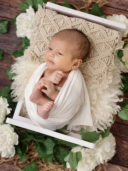 An awake and curious newborn, swaddled in white, looks up from a cozy bed of fur and flowers. Capturing these moments of quiet alertness is just as special as the sleepy ones.