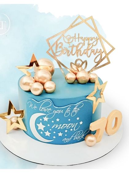 "We love you to the moon and back." A celestial-themed 70th birthday cake in blue and gold, decorated with stars and a crescent moon.