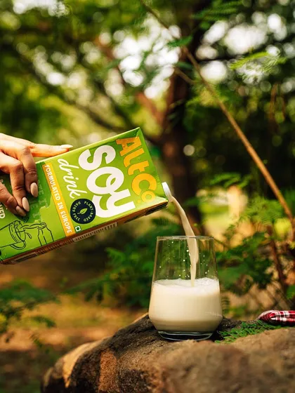 A refreshing pour of Alt Co. soy milk in a lush, green outdoor setting. This shot reinforces the brand's "plant-powered" message by visually connecting it with nature.