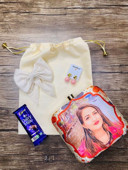 A sweet Rakhi combo for your sister. This set includes a personalized clutch with her photo, earrings, a bow clip, and chocolate.