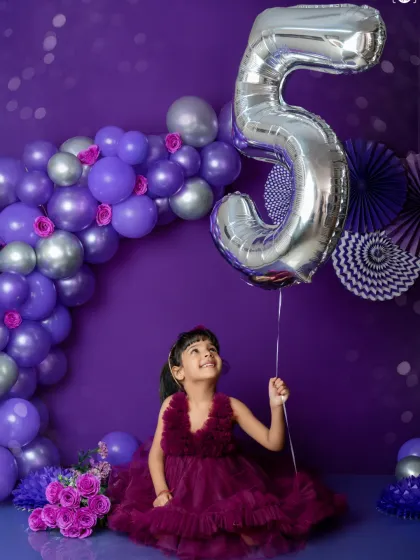 Five and fabulous. This young lady celebrates her fifth birthday in a sea of purple and silver, looking up at her giant number 5 balloon with wonder.