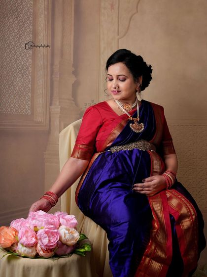 A regal studio portrait of a mother-to-be in a traditional Maharashtrian-style nauvari saree, seated with floral props.