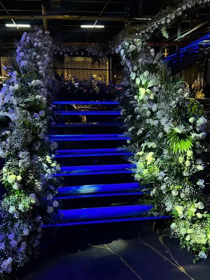 A dramatic staircase entrance for an engagement party, with the stairs illuminated in blue and flanked by cascading arches of baby's breath and white flowers.