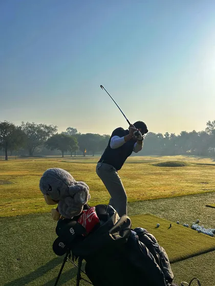 A golfer's follow-through is captured, with a cute headcover peeking out of the golf bag in the foreground.